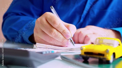 Insurance specialist calculating compensation and filling claims form at desk. Close up on hands, yellow toy car on table, shallow depth of field, natural daylight. 