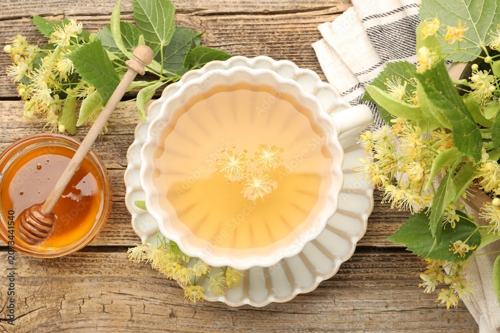 Obraz premium Delicious linden tea in cup, honey, leaves and flowers on wooden table, flat lay