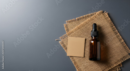 A brown glass bottle with a dropper on burlap and a blank note