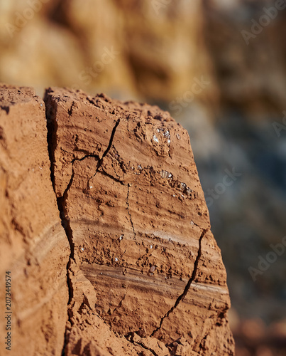 Vertical composition. Macro close-up shot of freshly chipped face of a terracotta clay sample. Surface reveals intricate mineral inclusions, small quartz crystals with a slight moist sparkle, and defi