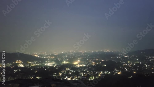 Aerial drone panning shot showing Dehradun town from Mussoorie town at night with soft haze fog and all the buildings in the distance surrounded by Himalaya mountains