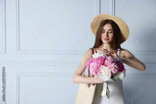 Woman with bouquet of beautiful peony flowers near white wall indoors, space ...