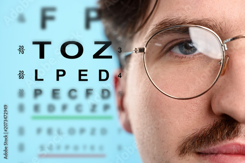 Obraz na plátně Man in glasses and eye chart on light blue background, selective focus