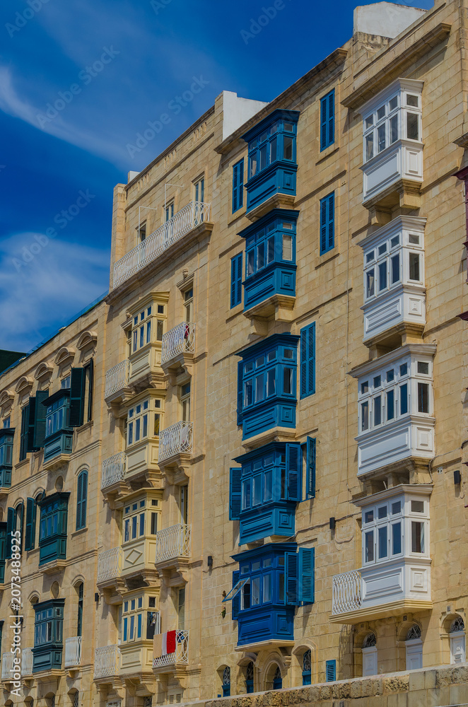 Fototapeta premium Traditional Maltese wooden balconies in Valletta Malta, colorful gallarija on limestone facade against blue sky, architecture
