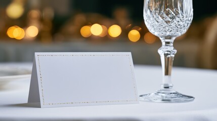 Elegant place card with gold border set on a white tablecloth next to a crystal glass