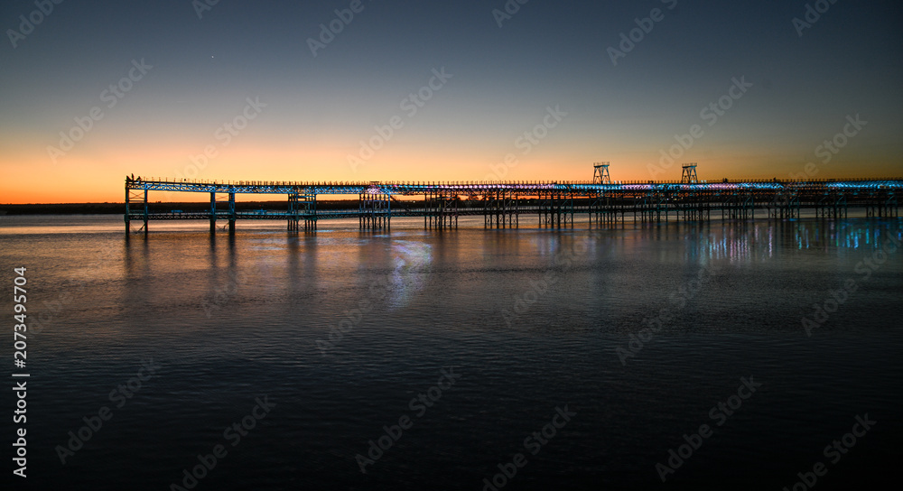 Fototapeta premium Illuminated mining pier over the Huelva estuary glowing in the golden hour
