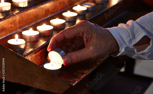 Fotografia Hand placing a tealight candle on a wooden altar with multiple lit candles, crea