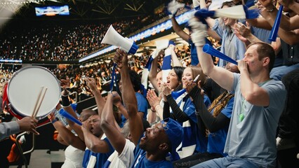 Passionate football capo beating drum and directing blue supporter, group from stadium stands during coordinated chant at live soccer match.