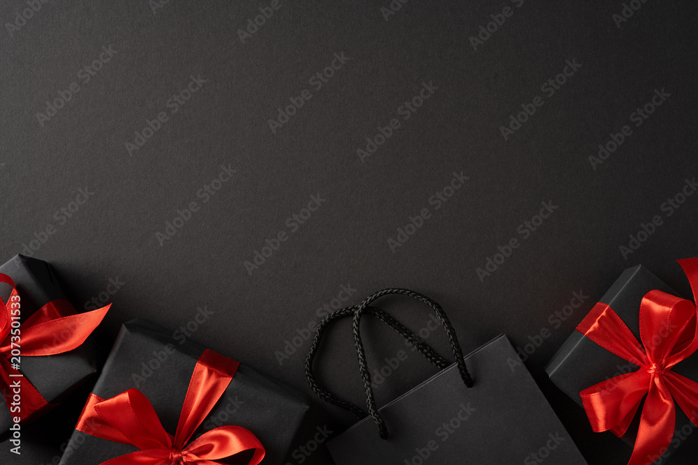 Fototapeta premium Black Friday and Cyber Monday black gift boxes with red bows and shopping bag on dark background
