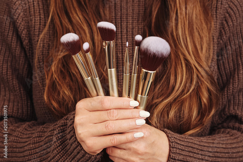 Woman holding professional makeup brushes in hands. Beauty accessories for cosmetic application and daily makeup routine. Background with female lifestyle skincare and personal care concept.