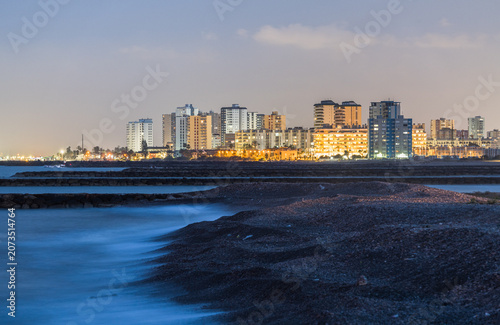 Long Exposure Rocky Coast with Silky Water and Illuminated City Skyline at Night