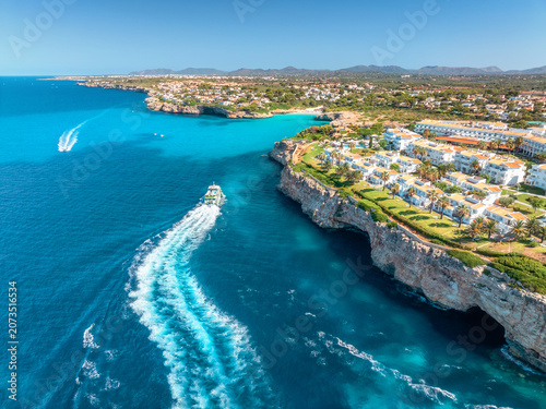 Canvastavla Aerial view of a white coastal resort with villas, palm trees on rocky cliffs above turquoise Mediterranean sea, boats on blue clear water