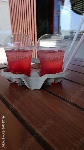 Two cups of refreshing red beverage in a carrier on wooden table  