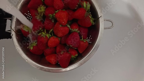 Fresh strawberries being rinsed in a colander under running water  