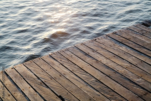 Wooden pier over calm sea water with shimmering sunlight reflection.