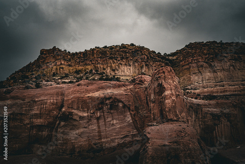 Bild auf Leinwand Dramatic desert cliffs with layered sandstone under a stormy sky, showcasing rug