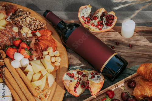 Bottle of red wine with cheese plate, fruits, walnuts, bakery, cured meats, berries on table with textile for an outdoor in a vineyard celebration. Winery, wine production, tonning, top view