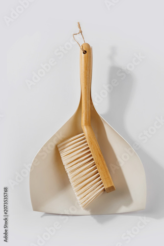 Vertical composition of bamboo cleaning brush with rope handle placed on dustpan highlighting sustainable materials and minimal design
