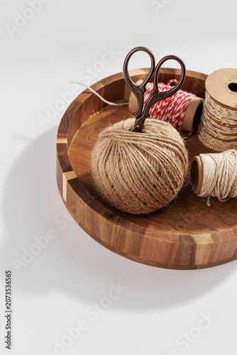 Twine ball with vintage craft scissors and decorative string spools arranged in wooden tray on light background, rustic diy craft and packaging supplies concept