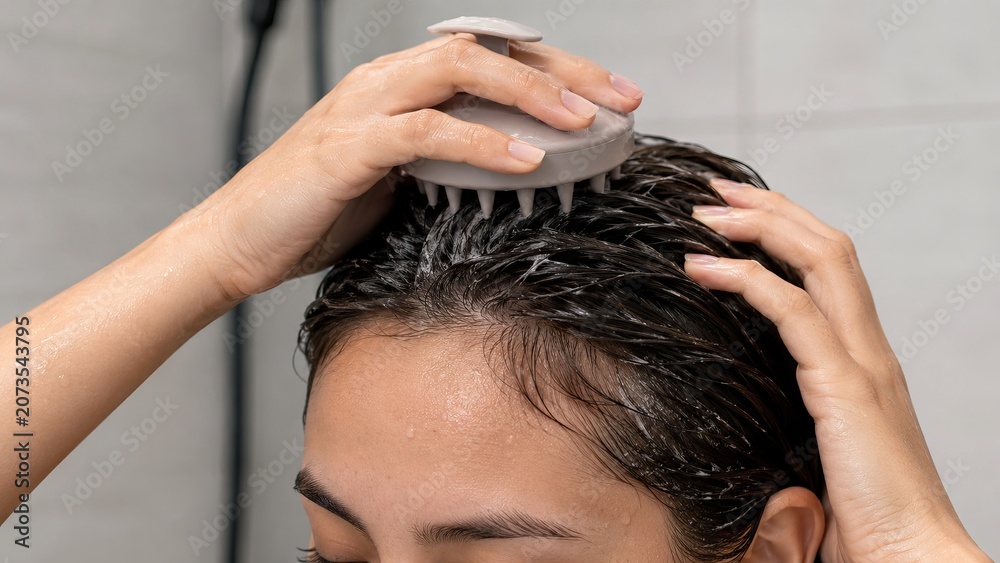 Fototapeta premium Woman using silicone scalp massager brush to wash hair in shower. Concept of hair care routine, scalp health, deep cleaning and hair growth massage treatment for healthy hair at home