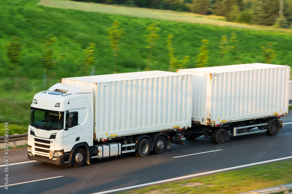 Obraz premium White Semi-Truck Hauling Double Shipping Containers on Highway Route, The Concept of Intermodal Freight Logistics