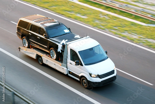Quadro su tela Tow Truck Transporting Second-Hand Used Black SUV Car on Highway, The Concept of