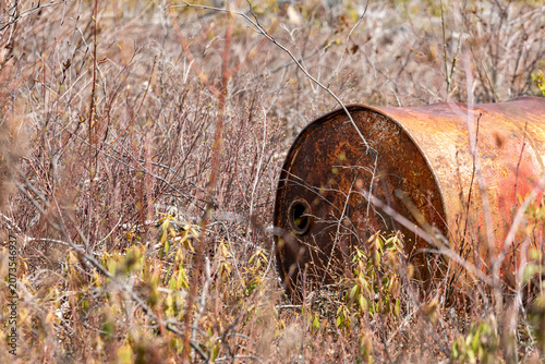 Obraz na plátne Parents, Quebec, 20 May 2026 : A rusty metal barrel lies abandoned in dry, overgrown brush and sparse vegetation