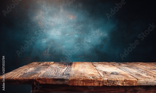 A rustic wooden table sits prominently against a textured, teal-blue background, creating a moody and artistic studio setting.