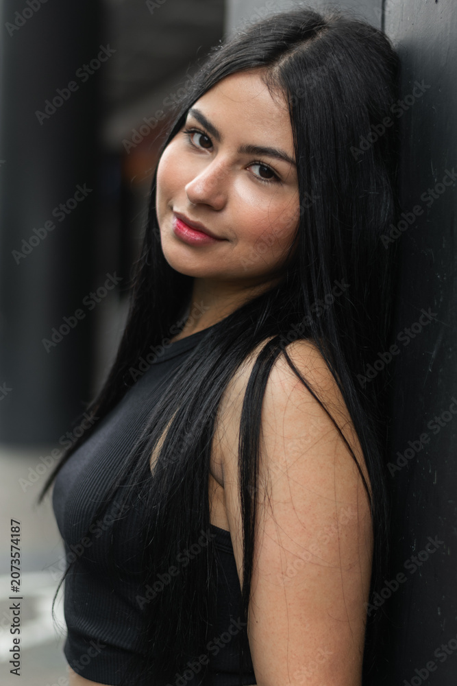 Fototapeta premium Close portrait of smiling young Latina woman in black outfit on urban street