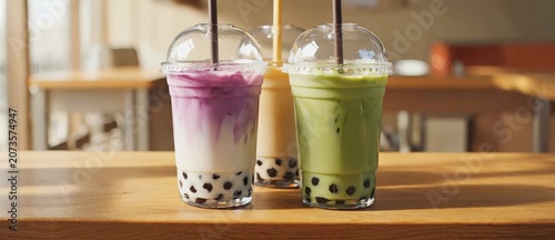 Three colorful bubble tea beverages with straws on wooden table indoors