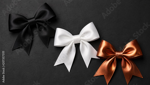 Three decorative bows in black, white and gold colors on dark background