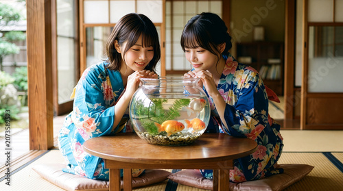 和室のテーブルに置かれた金魚鉢を笑顔で見つめる浴衣を着た女性たち