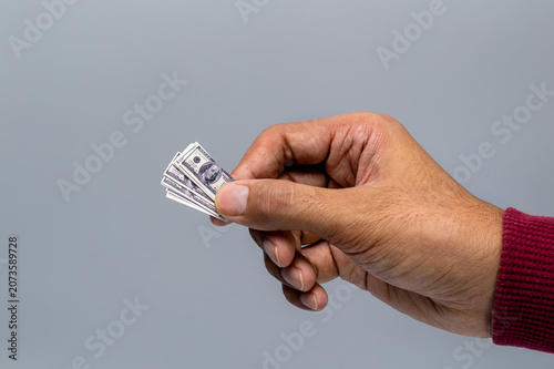 Close-up of a human hand holding tiny, miniature US dollar bills against a gray background. Inflation, low purchasing power, shrinking value of money, tight budgets, shrinkflation concept.