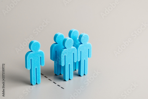 Photos A group of blue human figures separated from a single individual figure on a gray background
