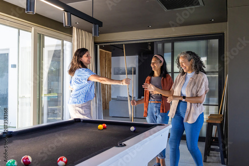 Diverse female friends playing pool, holding cues in home game room with black felt table