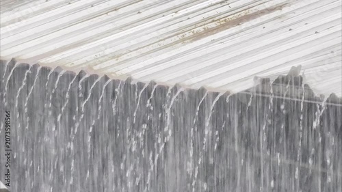 Heavy rain falling on a corrugated metal roof creating a curtain of water.