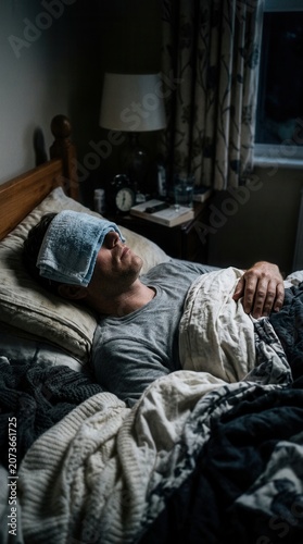 Unwell Person Resting In Bed With Cool Compress On Forehead