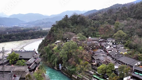 A historic water conservancy site lies by a winding river, with traditional buildings and forested mountains in the backdrop.