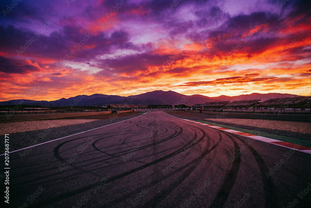 Fototapeta premium Dirt Road Winding Through Desert Landscape at Dramatic Sunset with Silhouetted Tracks