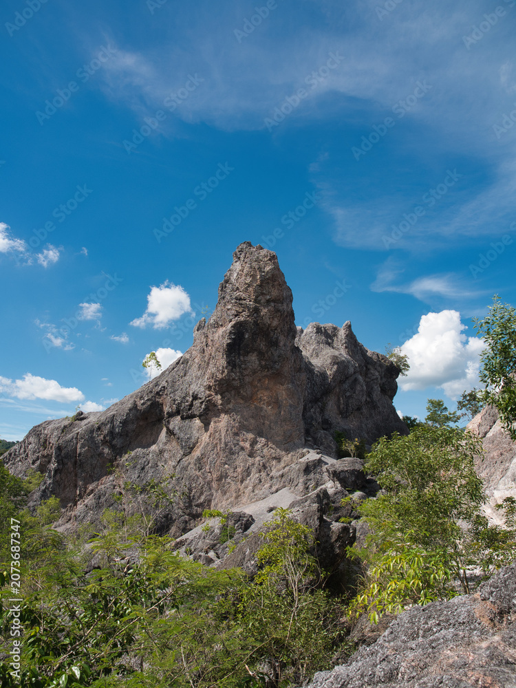 Fototapeta premium Landscape of a stone quarry or limestone cliff features sparse vegetation trees sand clouds, and a bright blue sky.