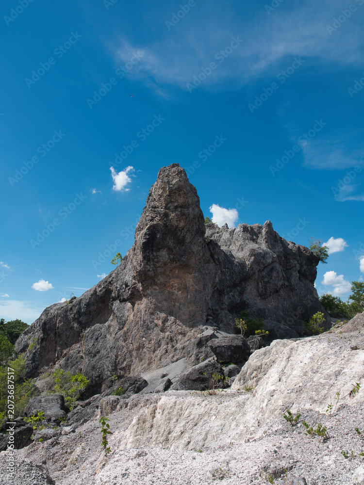 Fototapeta premium Landscape of a stone quarry or limestone cliff features sparse vegetation trees sand clouds, and a bright blue sky.