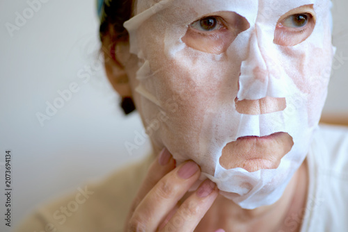 Elderly woman applying hydrating sheet mask during home skincare beauty routine
