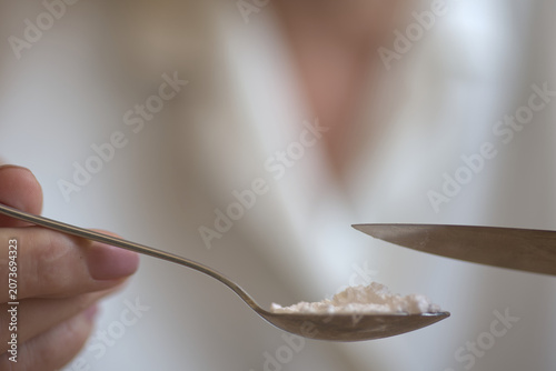 Woman flattening the creatinine powder in a teaspoon with a kitchen knife to measure three grams for intake