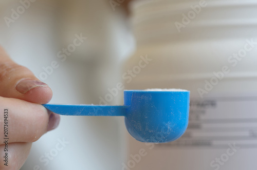 Person preparing a creatine powder drink, holding a blue measuring scoop