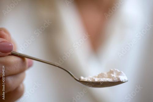 Hand holding teaspoon of creatine powder supplement for preventing sarcopenia in the elderly