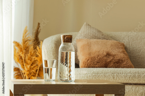 Foto Glass and carafe of water on wooden table in cozy living room