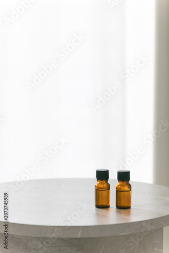 Two amber glass dropper bottles on a minimalist marble table, soft bright background with copy space for cosmetic or essential oil branding.