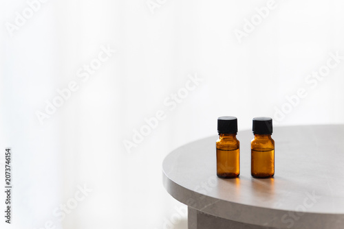 Two amber glass dropper bottles on a minimalist marble table, soft bright background with copy space for cosmetic or essential oil branding.