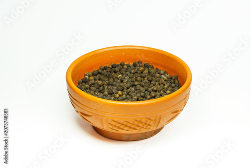 Fotografie A clay bowl filled with black peppercorns isolated on white background