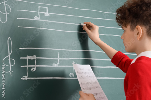 Teenage boy writing music notes on blackboard in classroom